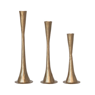 Three gold metallic candle holders of varying heights on a white background