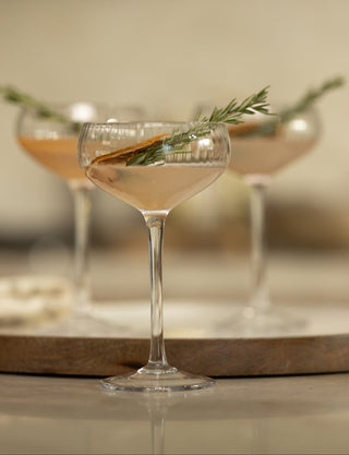 Cocktail in a glass with a sprig of rosemary on a wooden tray.