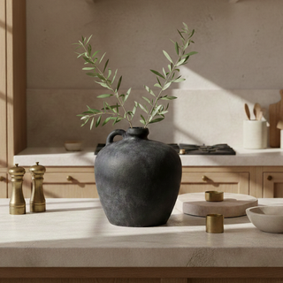 Black vase with green branches on a kitchen counter