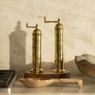 Pair of brass pepper mills on a wooden stand with a neutral background